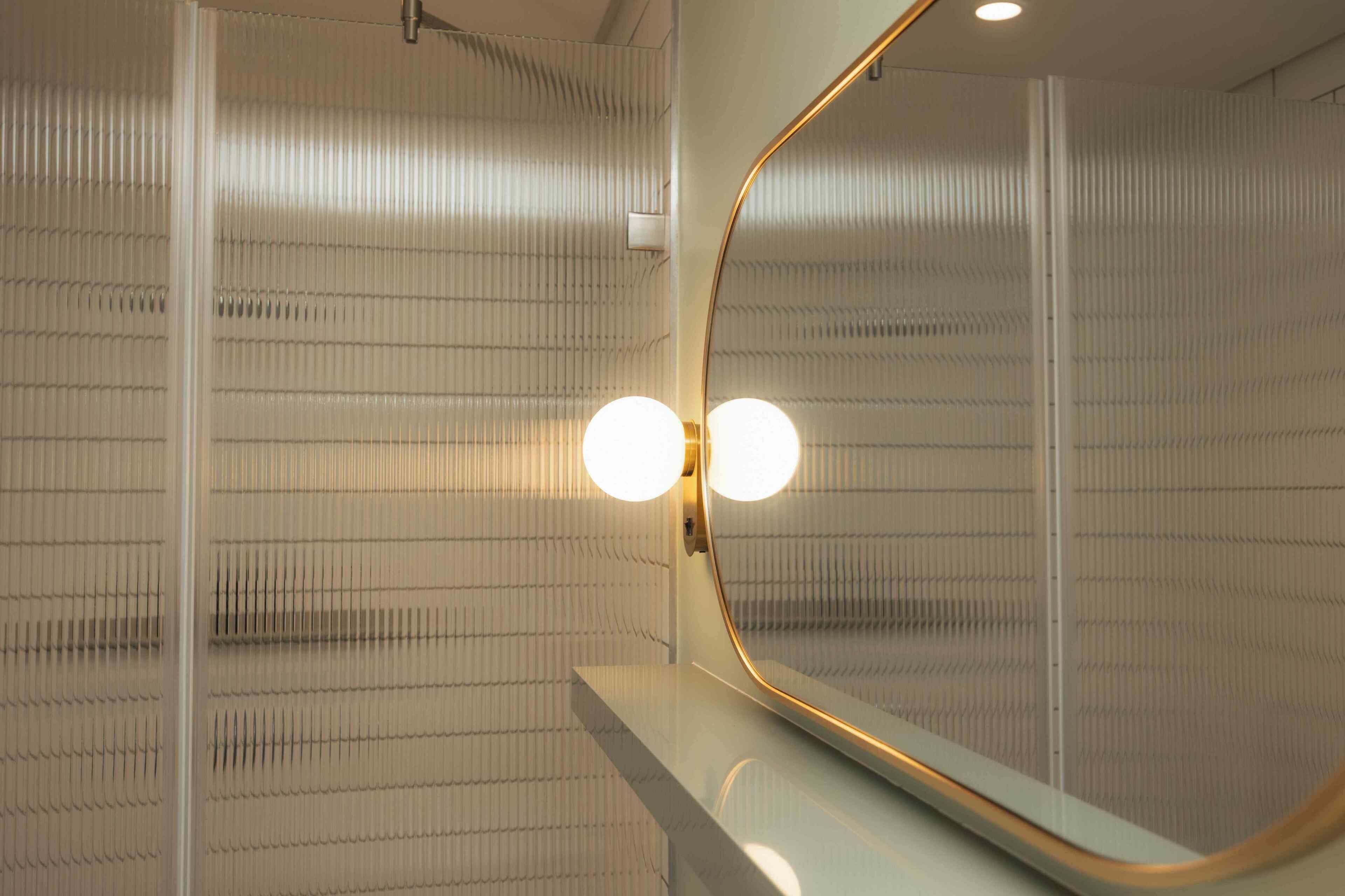 Une salle de bain avec un meuble-lavabo doté d’un miroir, un luminaire fixé au mur et un mur à texture.