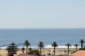 A beach view with palm trees, a sandy shore, and a clear sky. - ONEHUNDRED on M - Fluent Serviced Apartments (Cape Town)