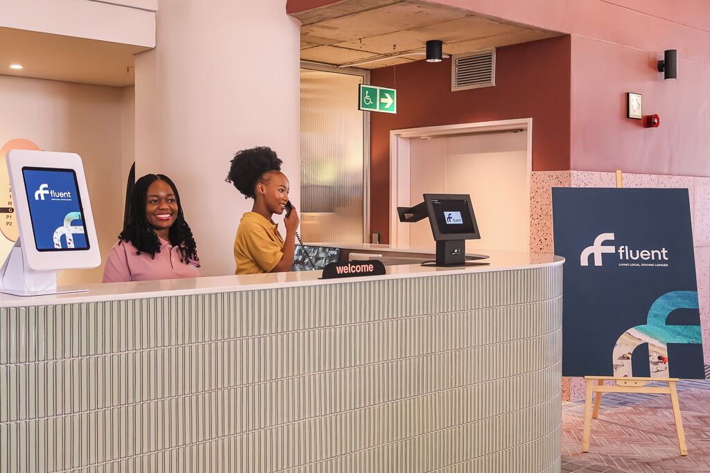 A reception area with a digital kiosk, a welcome sign, and a large poster of a chair.