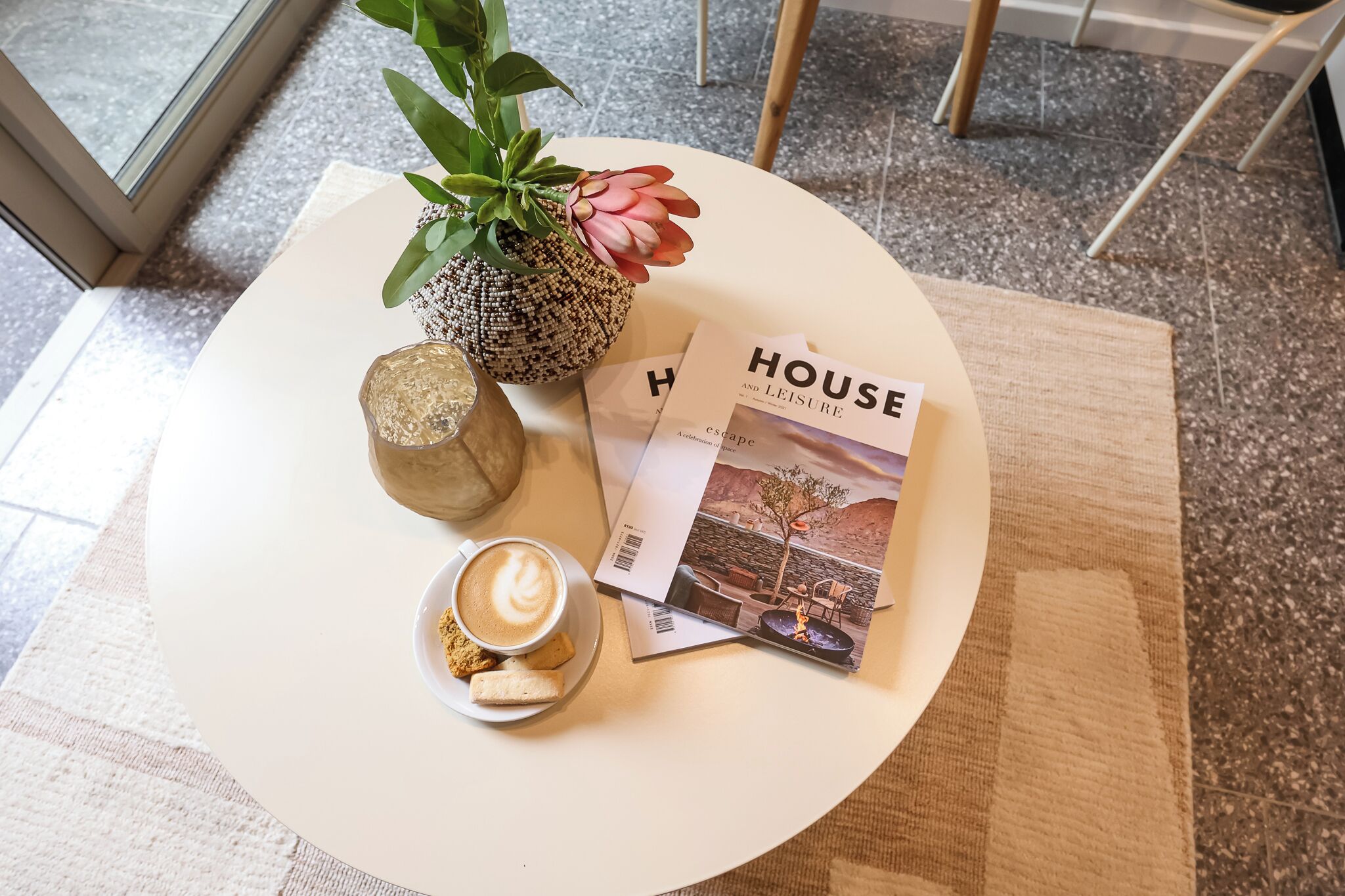 A white table with a magazine, a cup of coffee, a cookie, and a plant.