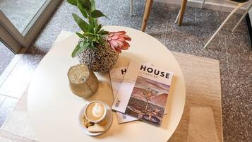 A white table with a magazine, a cup of coffee, a cookie, and a plant.