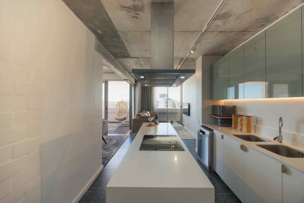 A modern kitchen with a central island, built-in appliances, and a large window providing natural light. - ONEHUNDRED on M - Fluent Serviced Apartments (Cape Town)