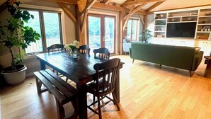 Un coin repas avec une table et des chaises en bois, un banc et une plante en pot. Une grande fenêtre laisse entrer la lumière naturelle et offre une vue sur l’extérieur.