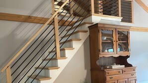 Un escalier en bois, doté de rampes en verre, mène au deuxième étage. On peut apercevoir, au deuxième étage, une armoire en bois avec des portes en verre.