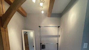 Une pièce avec des poutres en bois, un luminaire au plafond, un étagère en métal et un miroir.