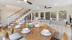 A modern dining area with a wooden table set for six, a staircase, and a view of the outdoors. - Sedona Canyon Whisper: A 3BR retreat in Oak Creek Canyon with stunning red rock views. (Sedona)