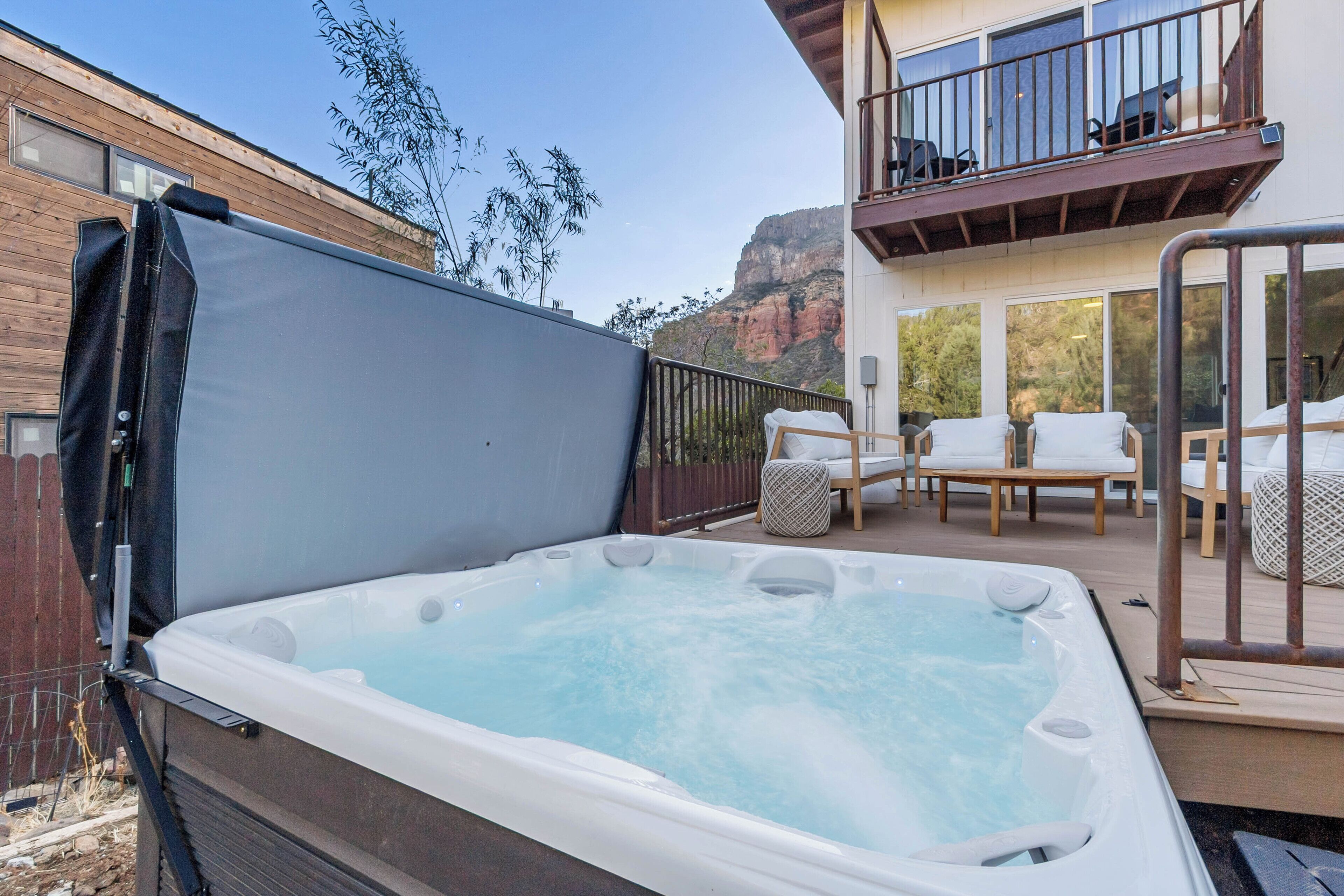 A hot tub on a deck with a view of a mountain and a wooden building.