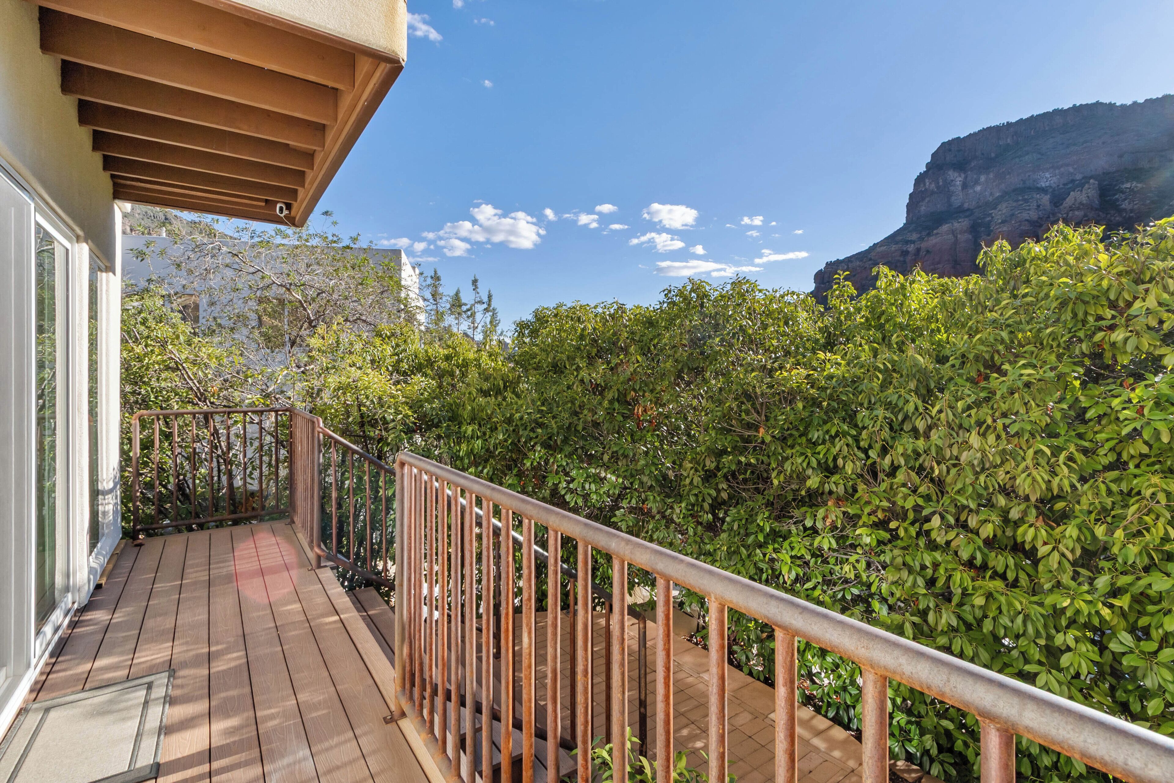 A wooden deck with a metal railing, overlooking a lush green landscape and a mountain in the background.