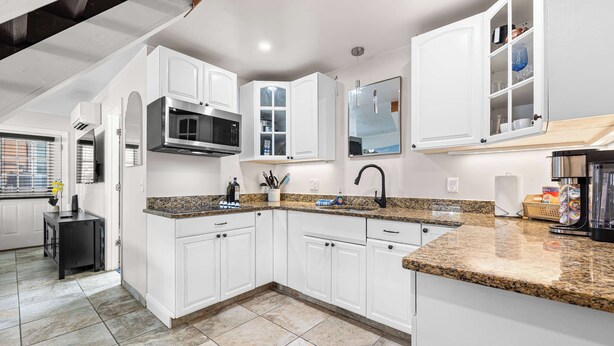 A modern kitchen with white cabinets, granite countertops, and a built-in microwave.