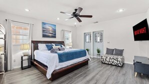 Une chambre moderne avec un grand lit, un ventilateur de plafond, une télévision et un bureau.