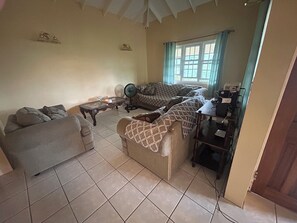 A living room with two sofas, a coffee table, a fan, and a window with curtains.