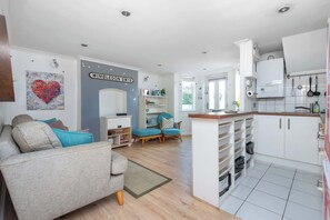 A modern living room with a sofa, a blue armchair, and a kitchen area with white cabinets and a built-in oven.