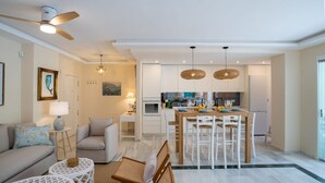 Una sala de estar moderna con sofá, sillas y una mesa de comedor. Hay una zona de cocina con refrigerador, estufa y mesa de comedor.
