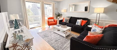 Uma sala de estar moderna com um sofá preto, uma poltrona laranja e uma mesa de centro branca.