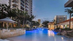 A swimming pool with a waterfall feature, surrounded by palm trees and modern buildings. - The Lookout-Level 33 (Surfers Paradise)