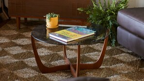 A round glass coffee table with a book and a potted plant on it, placed on a patterned rug. - The Artists Beach House Sea views (Lorne)