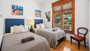 Ein Zimmer mit zwei Betten, einem Nachttisch mit Lampe, einem Sessel und einem Fenster mit Blick auf Grünflächen.