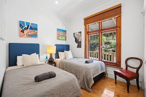 Una habitación con dos camas, una mesita de noche con lámpara, una silla y una ventana con vistas al verdor.
