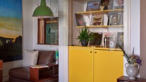 Ein Wohnzimmer mit einem gelben Schrank, einer grünen Pendelleuchte, einem braunen Ledersofa und einem Bild an der Wand.