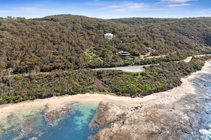 Un paisaje costero con una playa, aguas cristalinas y una colina arbolada.