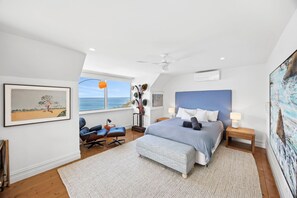 A bedroom with a large bed, a desk, a chair, a window with a view, and a ceiling fan. - The Artists Beach House Sea views (Lorne)