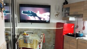 A dining area with a table set for two, a television mounted above the table, and a kitchen area with a red refrigerator and wooden cabinets. - Sea view terrace apartment (Arenzano)