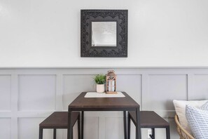 A dining area with a dark wooden table, two matching benches, a decorative mirror, a potted plant, and a lantern on a white placemat.