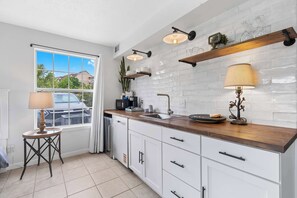 A modern kitchen with white cabinets, a wooden countertop, and a window with a view of houses.