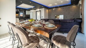 A modern dining area with a wooden table set for six, surrounded by upholstered chairs. - Villa Sunlegend (Yeşilköy)