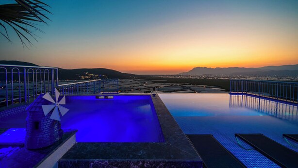 An infinity pool with a sunset view, a palm tree, and a blue-lit structure. - Villa Sunlegend (Yeşilköy)