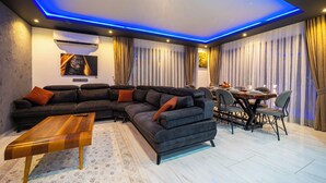 A modern living room with a sectional sofa, a wooden coffee table, and a dining area with a table and chairs. - Villa Sunlegend (Yeşilköy)