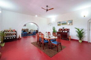 A dining area with a round table, chairs, a ceiling fan, and potted plants.