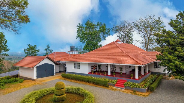 A two-story house with a red-tiled roof, a covered porch, and a circular garden feature.