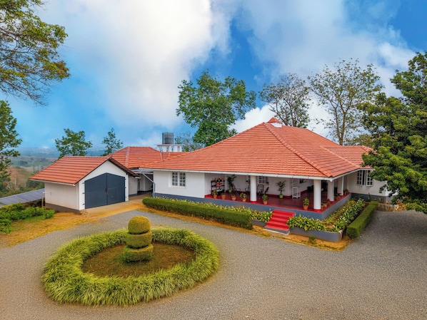 A two-story house with a red-tiled roof, a covered porch, and a circular garden feature.