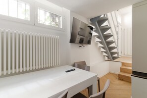 Un interior moderno con una mesa blanca, un televisor montado, un radiador y una escalera en espiral.