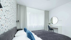 A modern hotel room with a bed, a desk, and a large window.