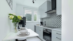 A modern kitchen with white cabinetry, a built-in oven, and a window with blinds.