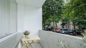 A balcony with a small table and chair, a potted plant, and a view of parked cars and trees.