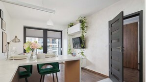 A modern kitchen with a white countertop, two green bar stools, a pendant light, and a large window.