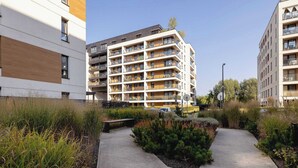 A modern apartment building with multiple balconies, a central courtyard with greenery, and a clear sky.