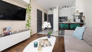 A modern living room with a flat-screen TV, a white console table, a sofa with a blue cushion, and a coffee table with magazines and a vase.