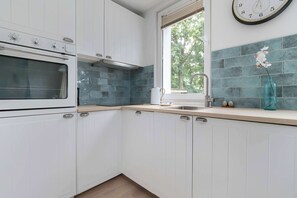 A modern kitchen with white cabinets, a built-in oven, a window with a view of greenery, and a clock on the wall.