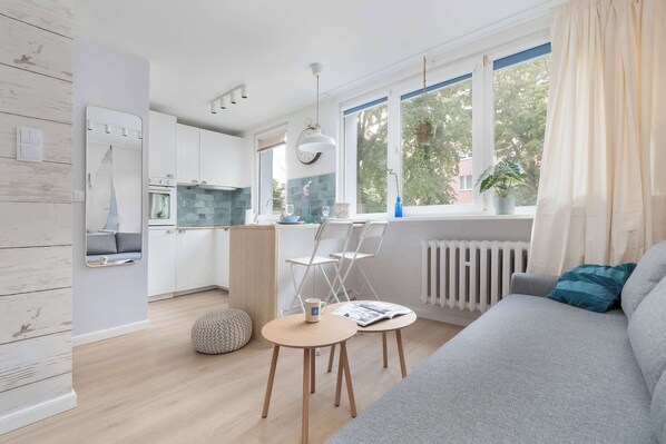 A modern kitchen with white cabinets, a dining area with a round table and chairs, and a large window with curtains.