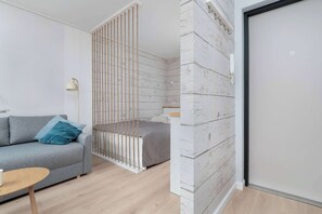 A modern bedroom with a grey sofa, a small round table, a bed with a grey bedspread, and a white wardrobe with a black frame.
