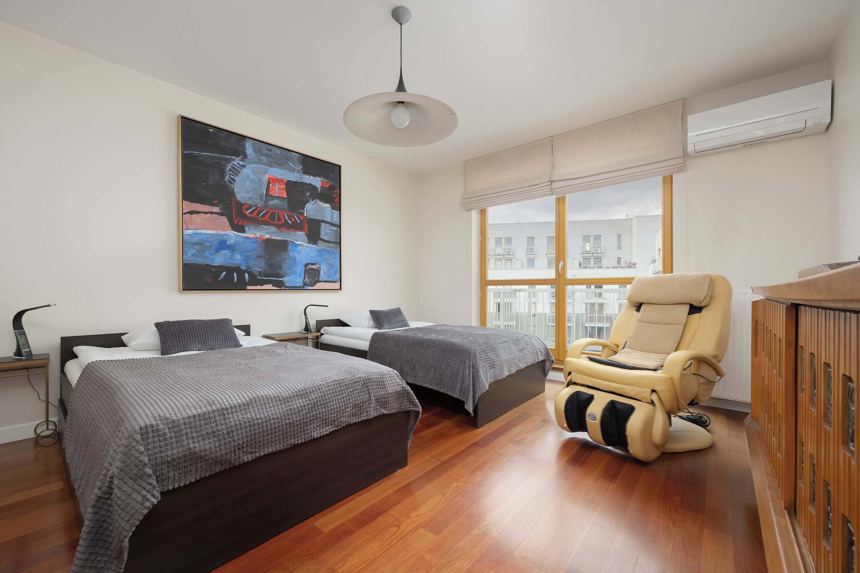 A modern bedroom with two beds, a massage chair, and a large window with a city view.