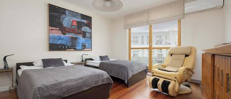 Un dormitorio moderno con dos camas, una silla de masaje y un amplio ventanal con vistas a la ciudad.