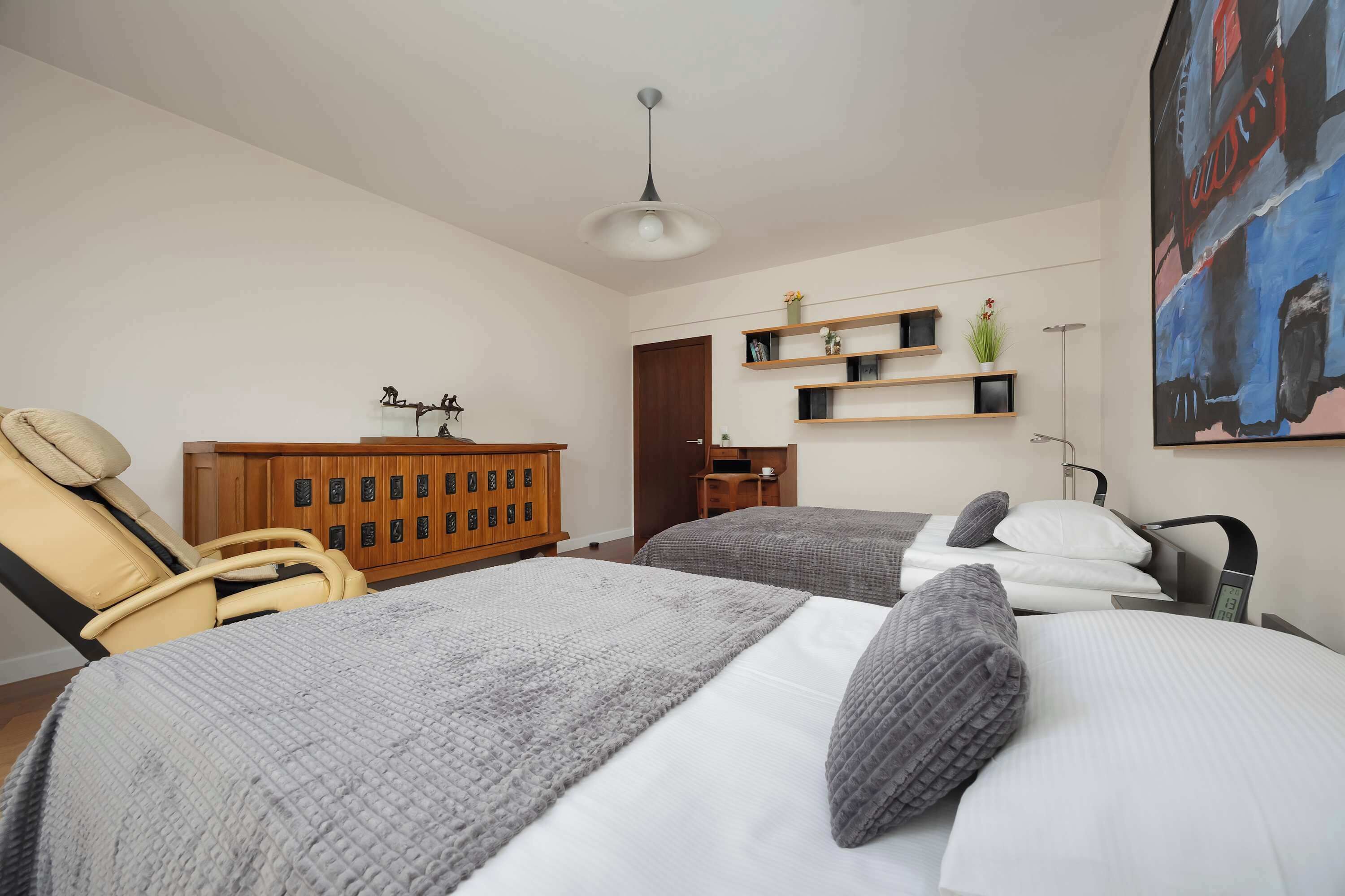 Un dormitorio moderno con dos camas, un armario de madera, una silla y un cuadro en la pared.