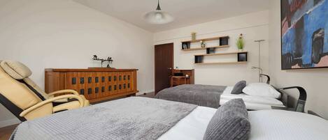 Un dormitorio moderno con dos camas, un armario de madera, una silla y un cuadro en la pared.