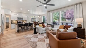 A spacious living area with a kitchen, dining area, and large windows offering views of trees.