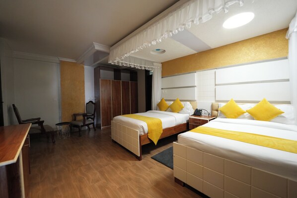 Habitación de hotel con dos camas, suelo de madera, un escritorio y un armario.
